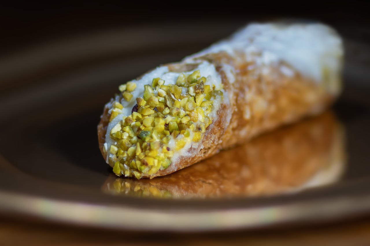 impact-img Close-up of a pistachio-topped cannoli pastry, showcasing the texture and vibrant colors.